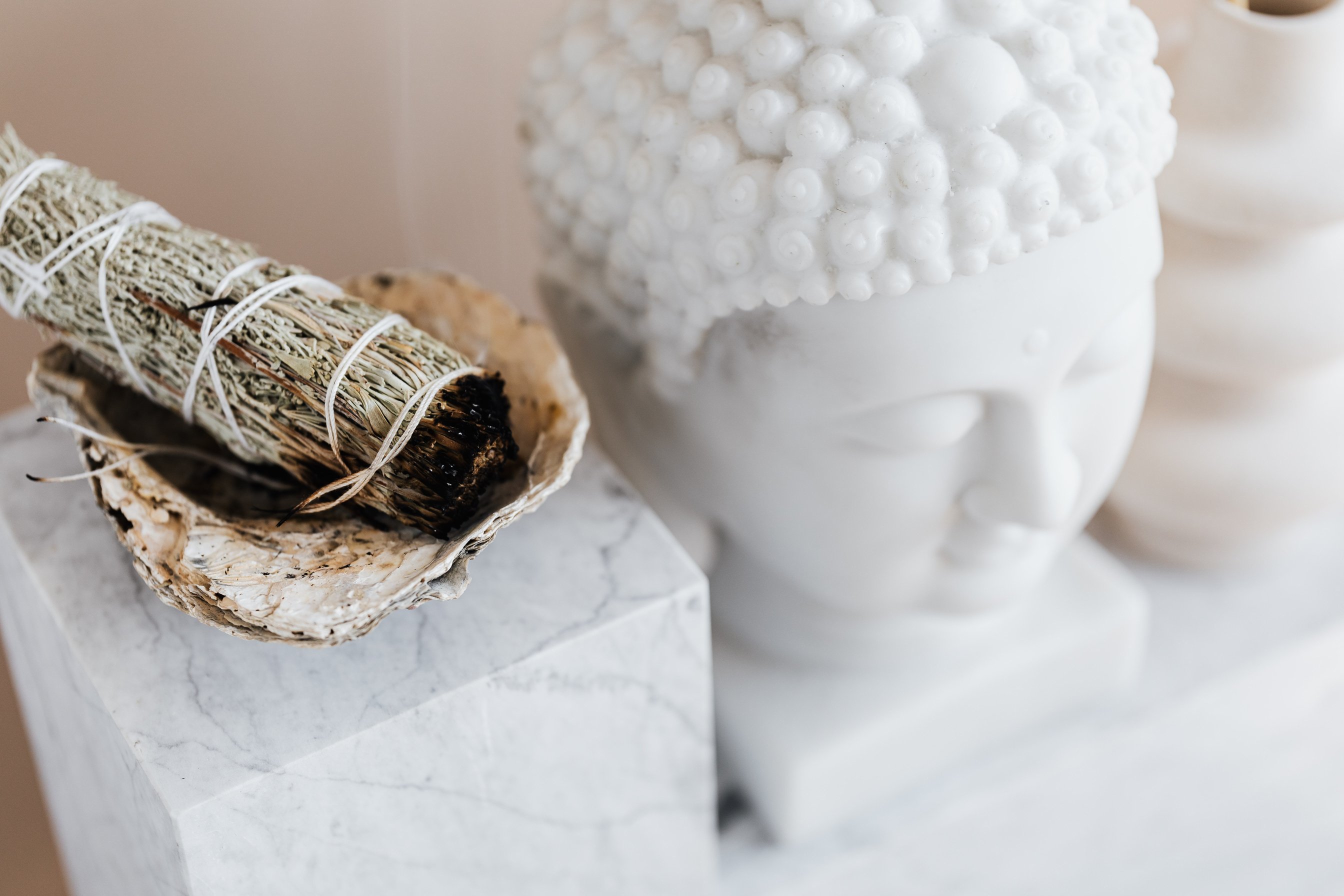 Sage smudge stick in bowl on marble shelf near Buddha head